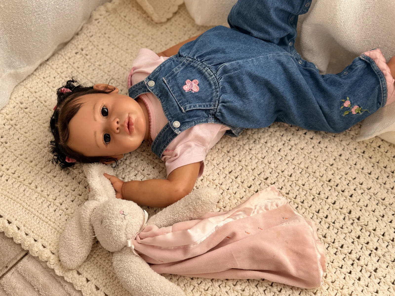 Reborn doll in embroidered denim overalls beside a soft bunny on a knitted blanket